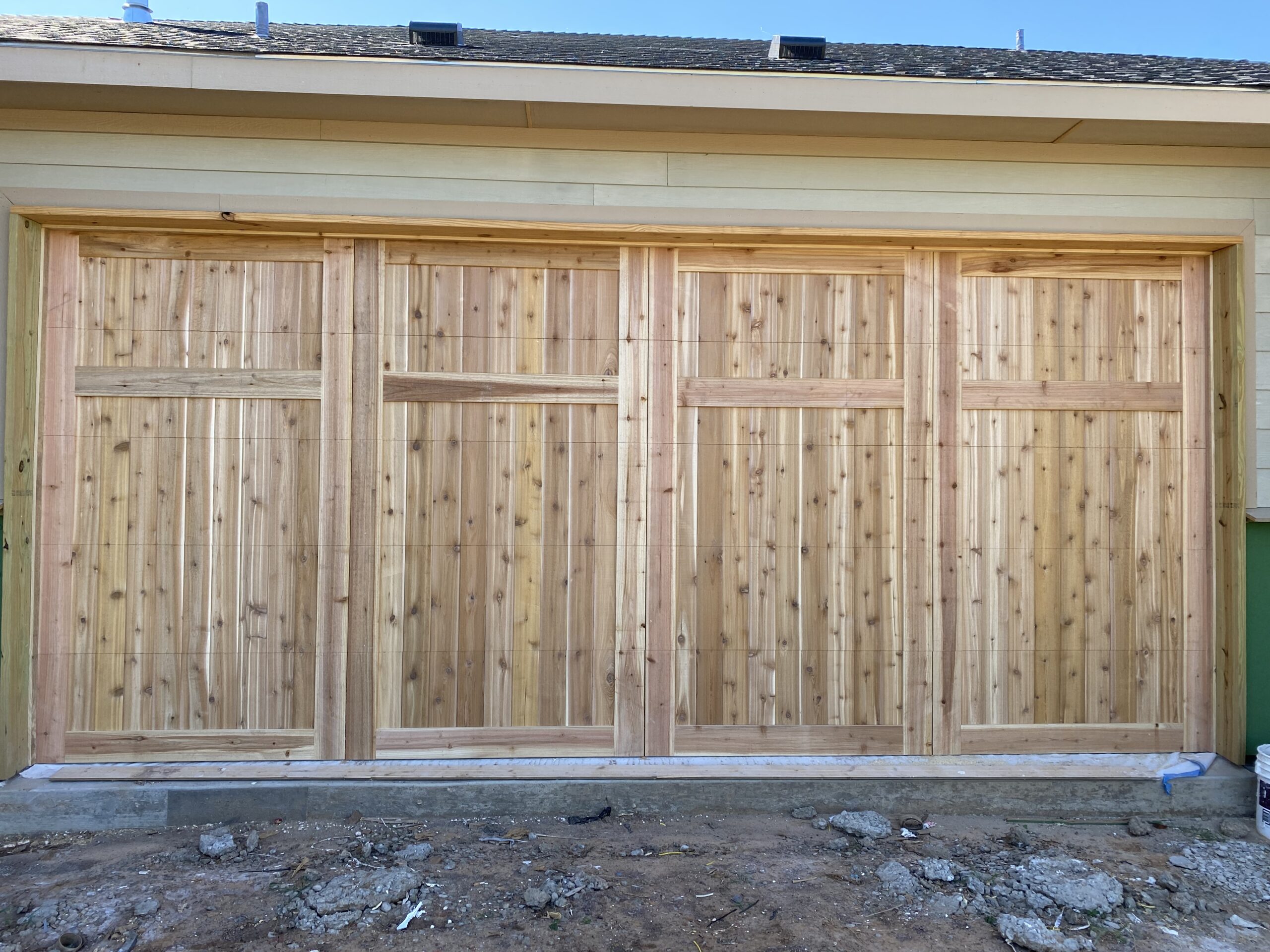 Custom wooden garage door under construction with a natural finish and vertical panel design.