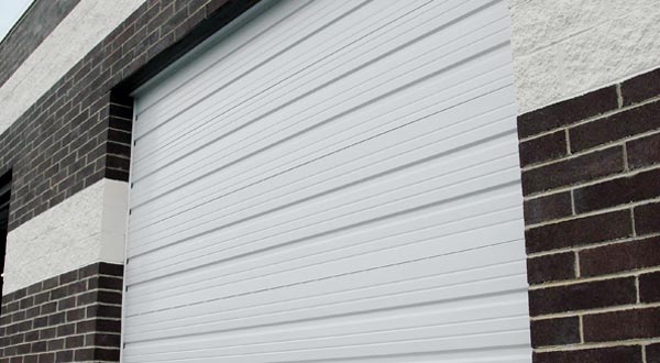 A white commercial roll-up door with horizontal grooves, partially open on a brick building.