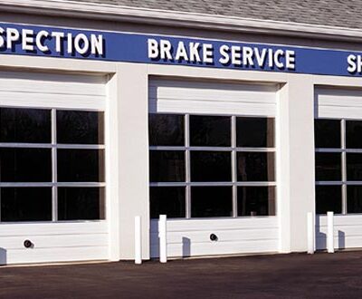 Three white commercial garage doors with windows, in front of a building that says "Inspection Brake Service Shocks"