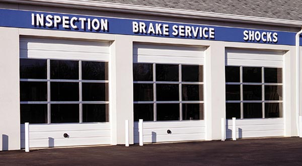 Three white commercial garage doors with windows, in front of a building that says "Inspection Brake Service Shocks"