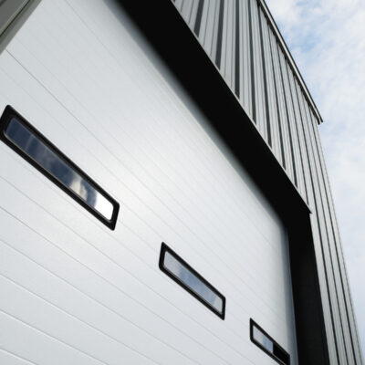 A close-up view of a large, modern industrial garage door with three small, horizontal rectangular windows, showcasing the sleek and minimalist design typical of the Amarr 2432 model.