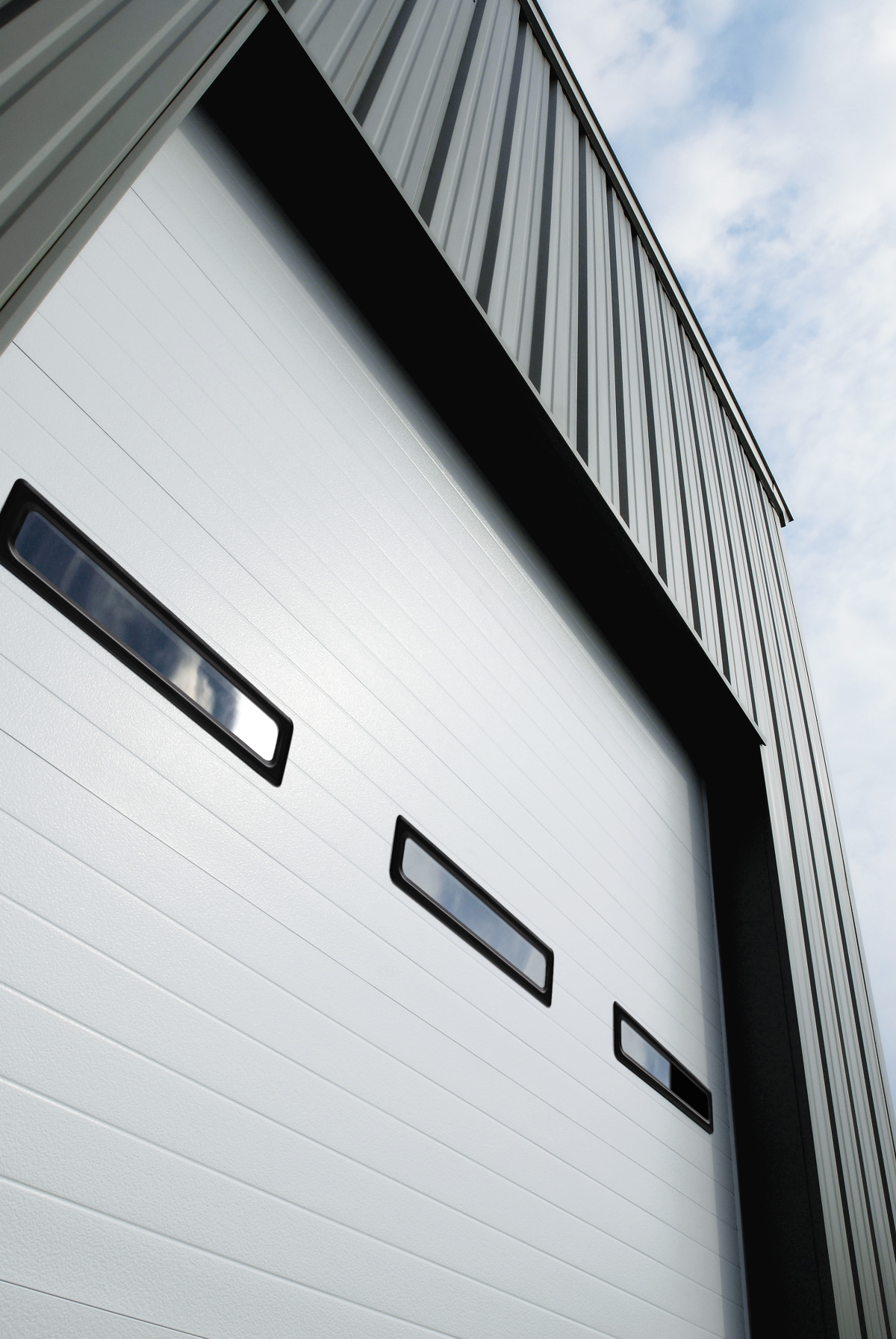 A close-up view of a large, modern industrial garage door with three small, horizontal rectangular windows, showcasing the sleek and minimalist design typical of the Amarr 2432 model.