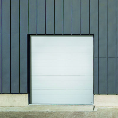 A white Amarr 2747 sectional garage door set in a modern building facade with dark gray vertical siding.