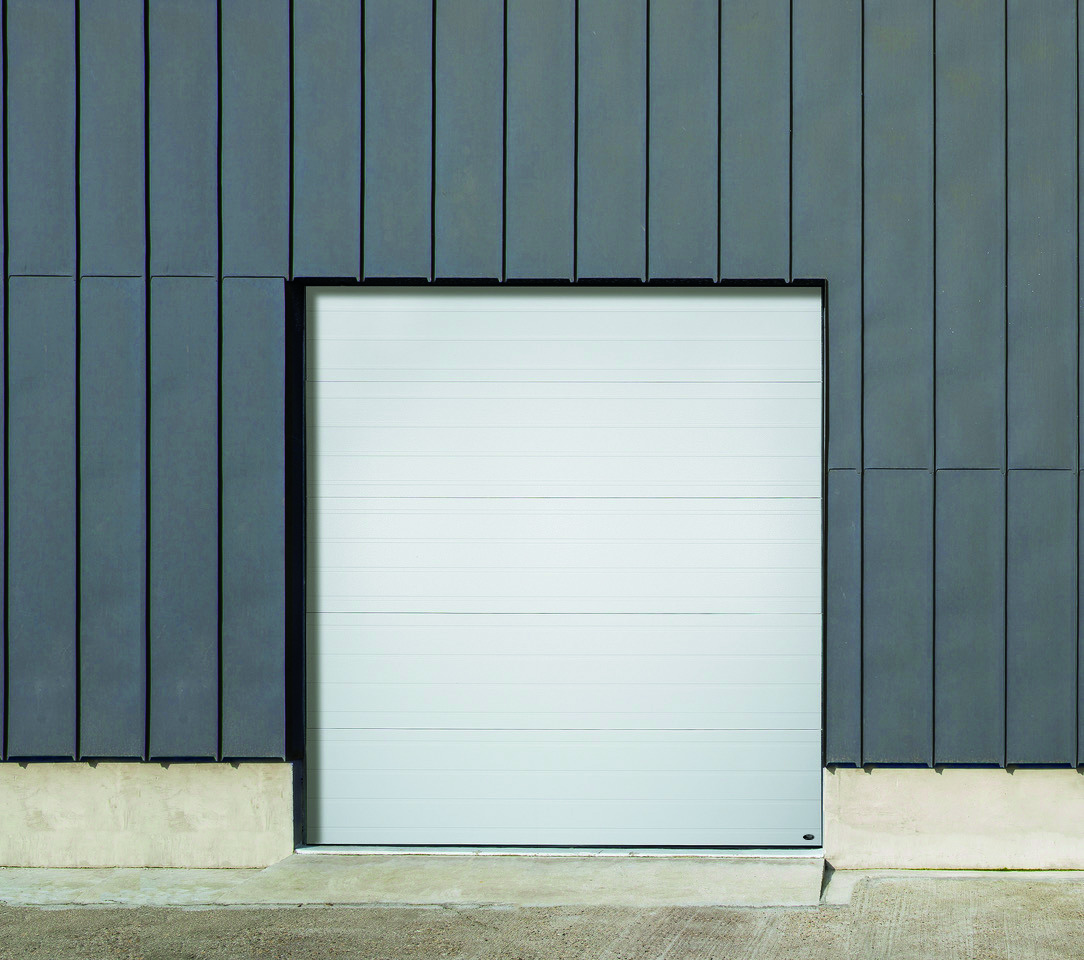 A white Amarr 2747 sectional garage door set in a modern building facade with dark gray vertical siding.