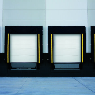 A row of four Amarr 2747 commercial loading docks with white sectional overhead doors and black dock levelers.