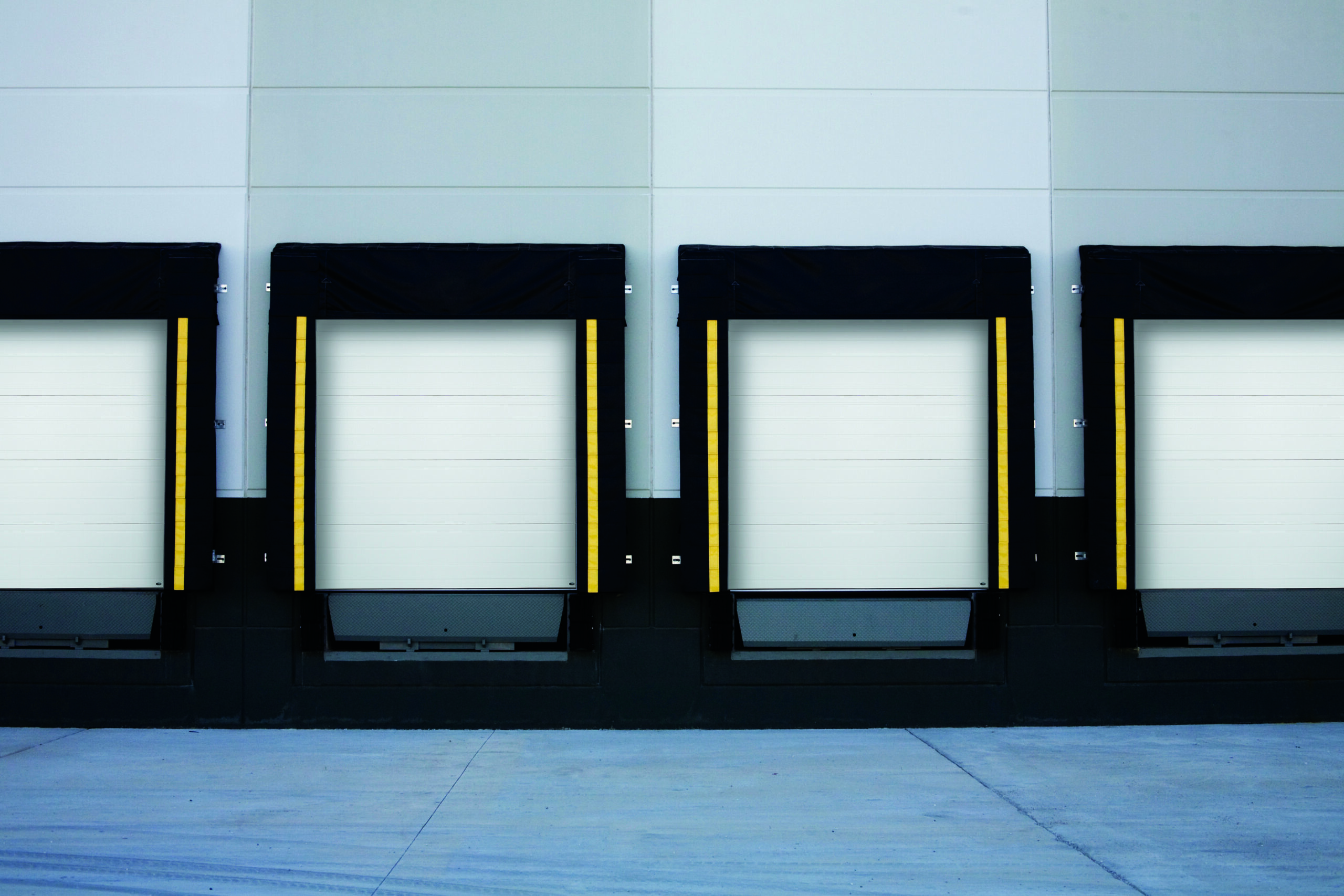 A row of four Amarr 2747 commercial loading docks with white sectional overhead doors and black dock levelers.