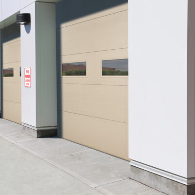 Modern commercial building exterior featuring multiple Amarr 2731 garage doors in a subtle beige color, each with small, rectangular windows offering a view of the countryside.