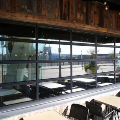 A large Clopay Architectural Series-Aluminum glass garage door with black frames opens onto a restaurant patio