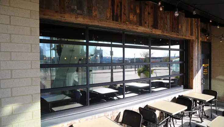 A large Clopay Architectural Series-Aluminum glass garage door with black frames opens onto a restaurant patio