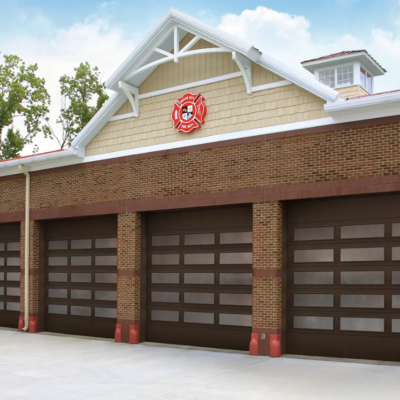 A brick fire station with four brown Clopay Architectural Series-Steel garage doors featuring windows