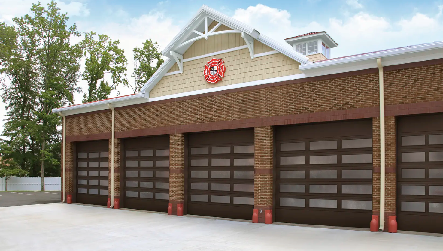 A brick fire station with four brown Clopay Architectural Series-Steel garage doors featuring windows