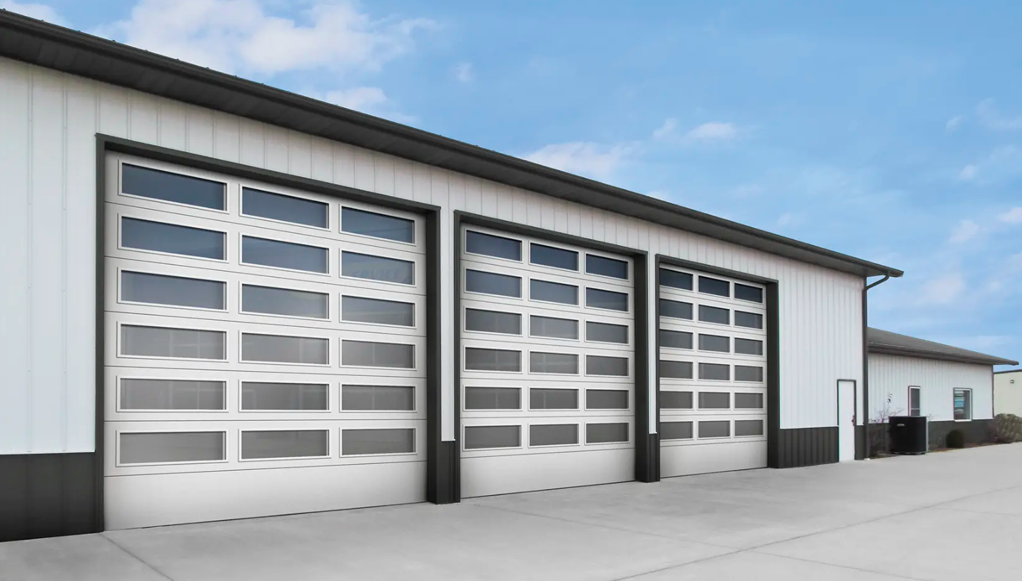 A modern metal building with three large commercial Clopay Architectural Series-Steel garage doors featuring multiple windows