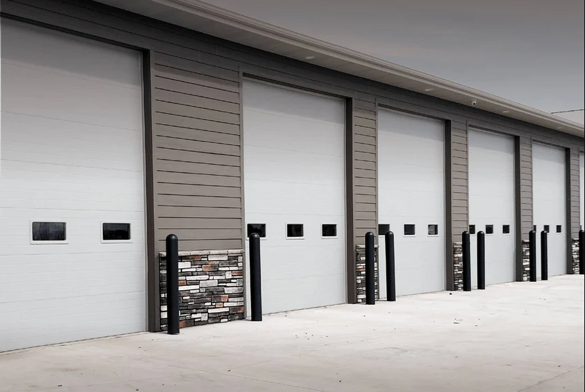 A large agricultural building with multiple white garage doors and green trim.