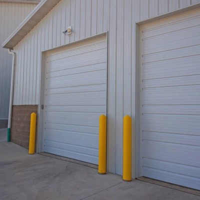 Two white commercial garage doors with a ribbed design, flanked by bright yellow protective bollards.