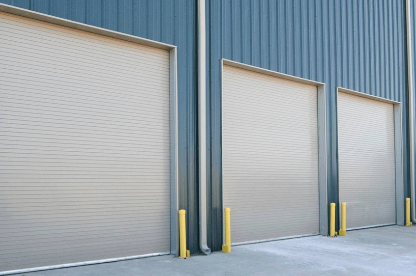 Three closed commercial roll-up doors in a row on a blue building.