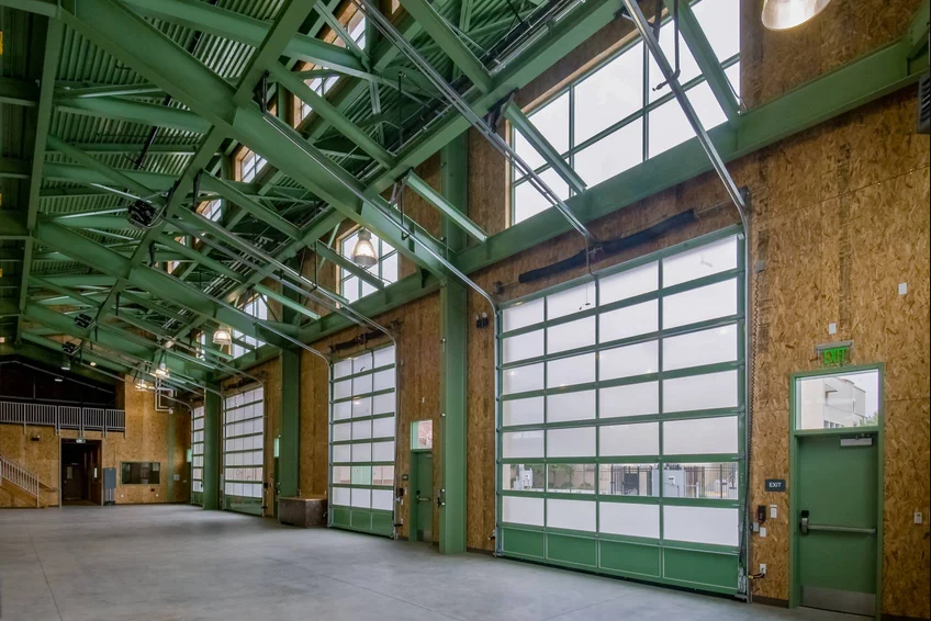 Interior of a fire station with large glass doors and green steel beams.