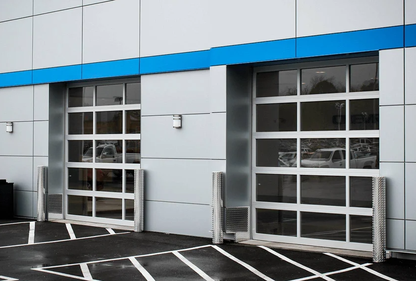 Two commercial glass garage doors with aluminum frames on a modern building exterior.