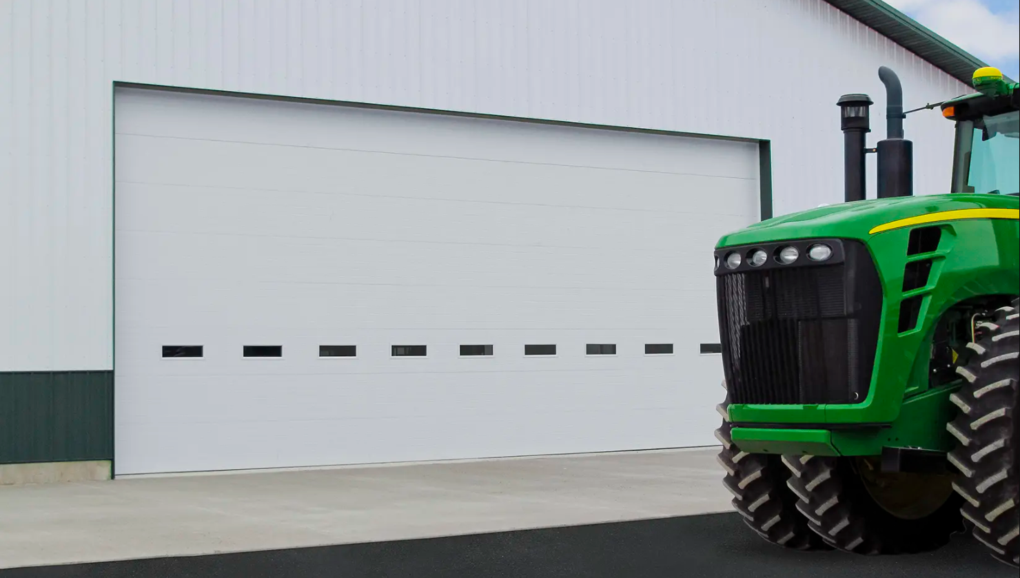 White commercial Clopay Energy Series garage door with windows, a green tractor parked in front