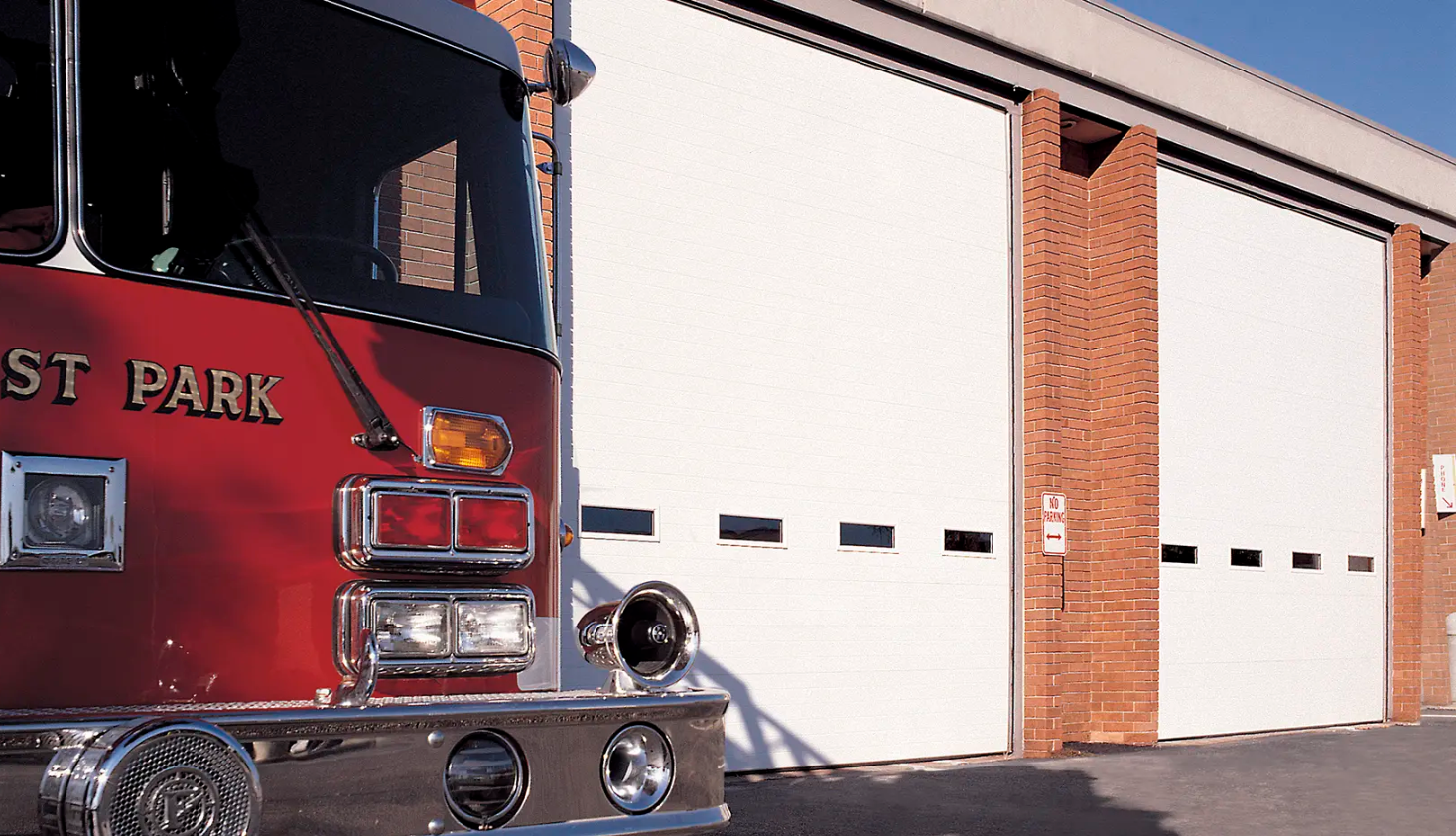 A red fire truck parked in front of a white Clopay Energy Series garage door at a fire station