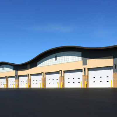 A commercial building with multiple white Clopay Energy Series with Intellicore garage doors and a curved roofline against a blue sky