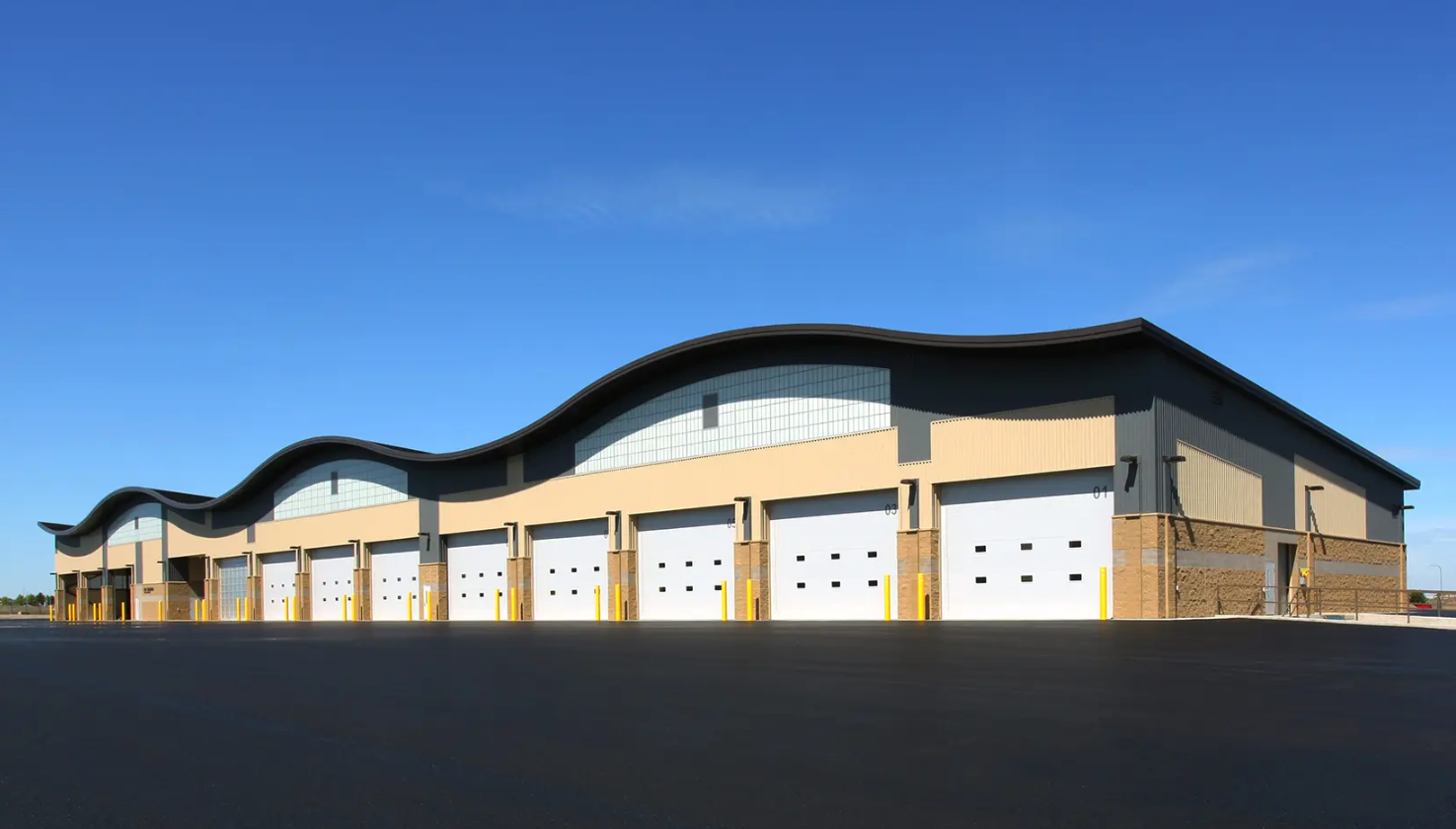 A commercial building with multiple white Clopay Energy Series with Intellicore garage doors and a curved roofline against a blue sky