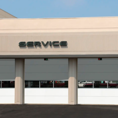 A commercial building with three white Clopay Energy Series with Intellicore garage doors and a sign that says "SERVICE" above them