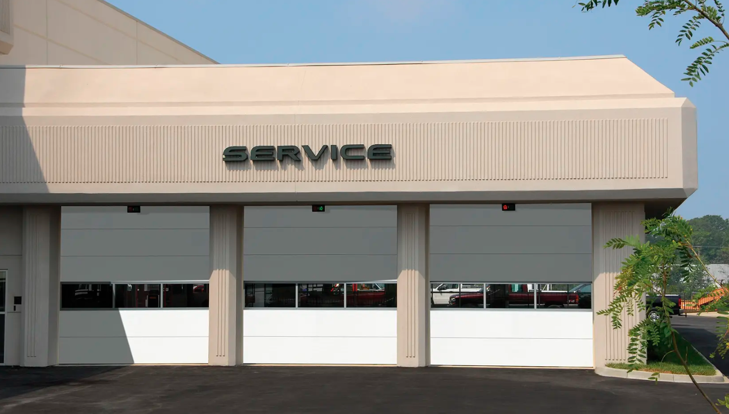 A commercial building with three white Clopay Energy Series with Intellicore garage doors and a sign that says "SERVICE" above them