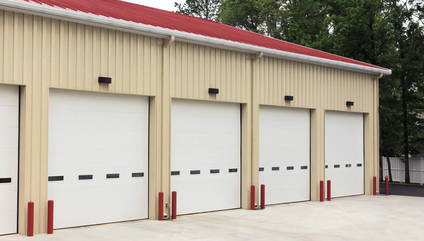 A row of white commercial Clopay Energy Series with Intellicore garage doors on a beige building with a red roof