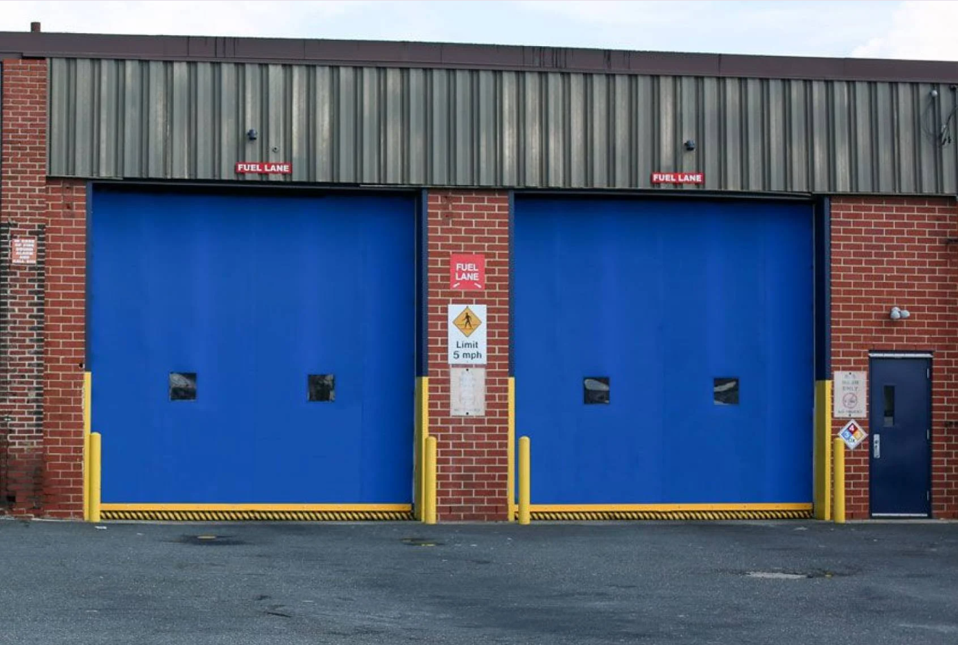 Two large blue industrial doors with yellow borders and warning signs.