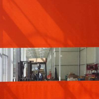 An orange high-speed roll-up door with a transparent window showing a warehouse interior with a forklift.