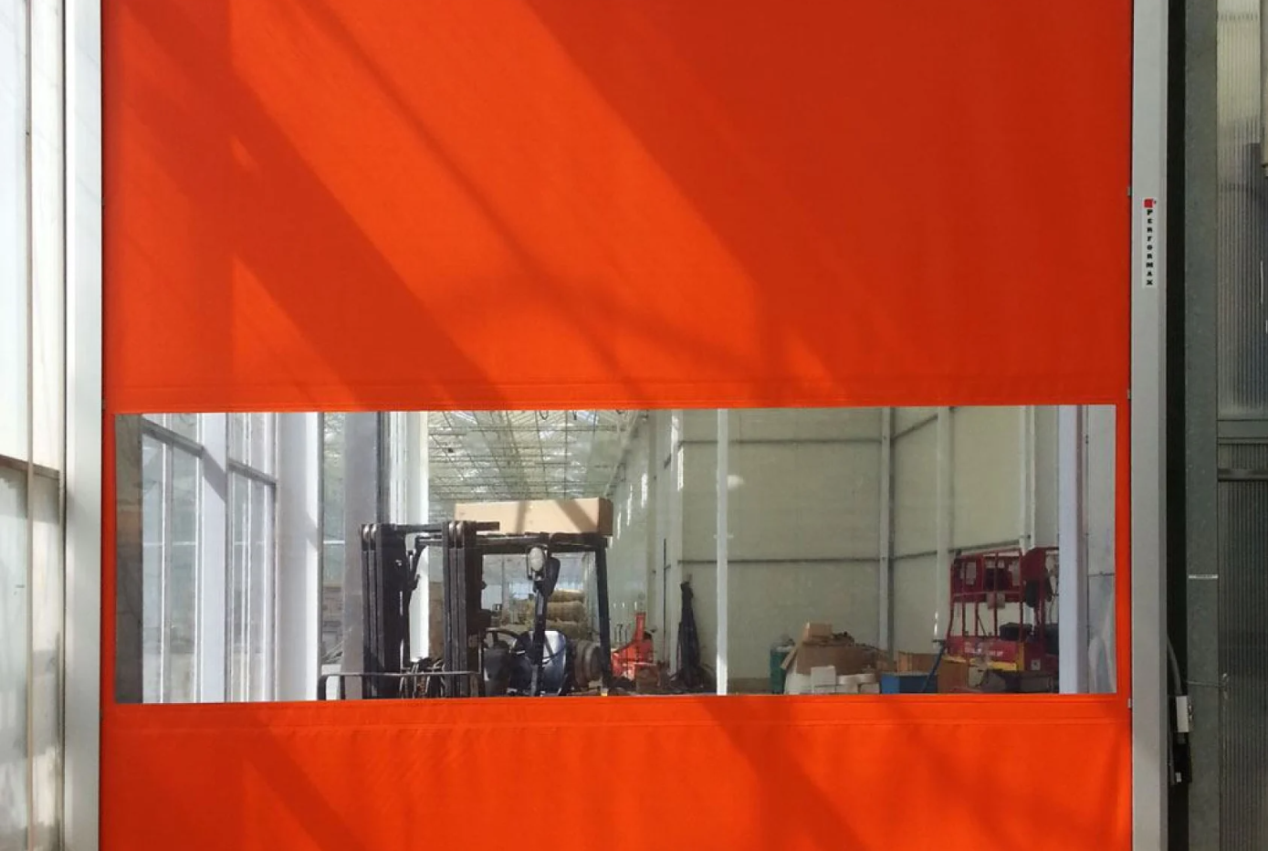 An orange high-speed roll-up door with a transparent window showing a warehouse interior with a forklift.