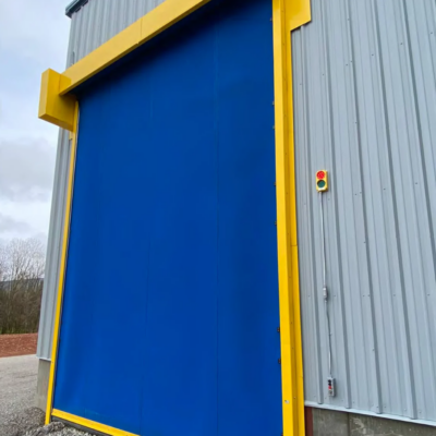 A large blue industrial high-speed door with a yellow frame on the exterior of a building.