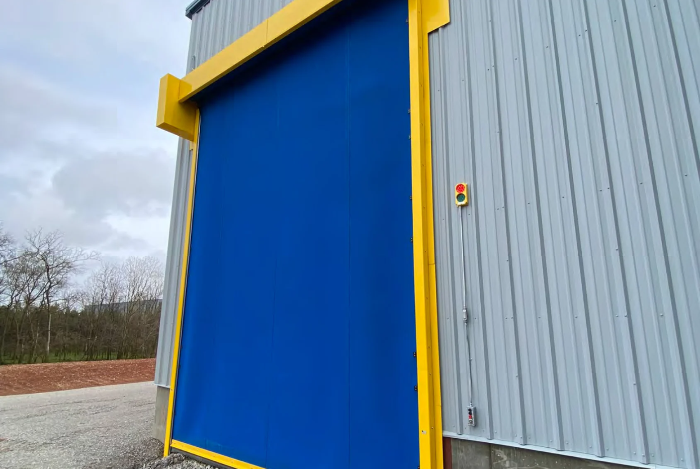 A large blue industrial high-speed door with a yellow frame on the exterior of a building.