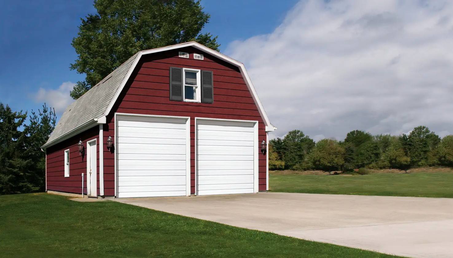 Red barn with white Clopay Industrial Series garage doors and a green lawn