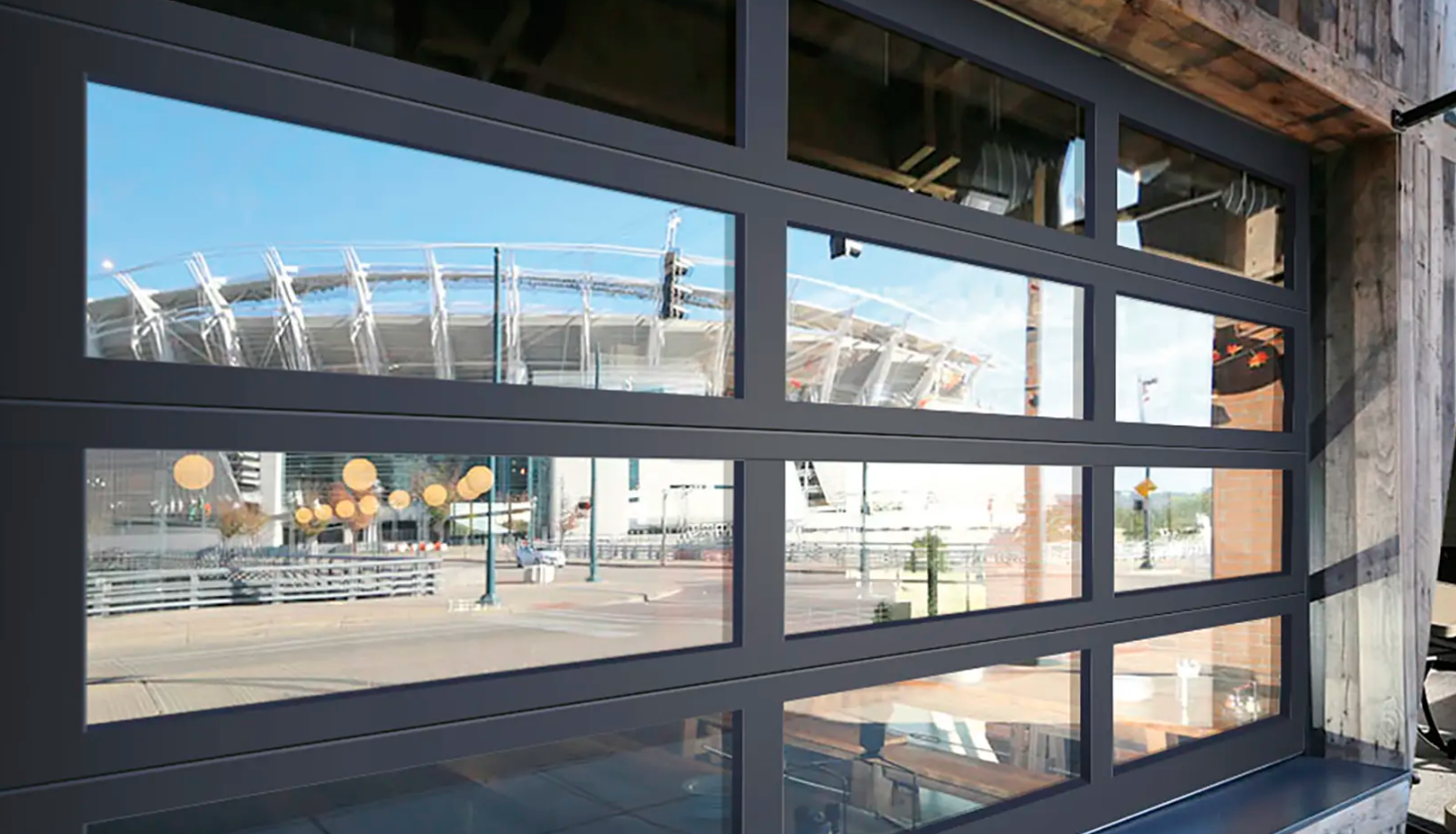 A commercial Clopay VertiStack Clear Door reflecting a cityscape with a stadium and clear blue sky