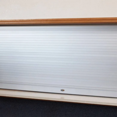 A closed silver roll-up security shutter with a wooden frame around it.