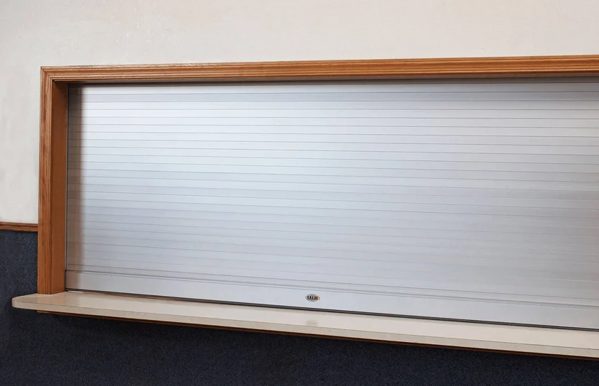 A closed silver roll-up security shutter with a wooden frame around it.