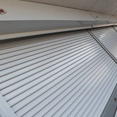 A large silver metal security roller shutter is partially open, showcasing its horizontal slats. The C.H.I. logo is visible on the housing unit above.