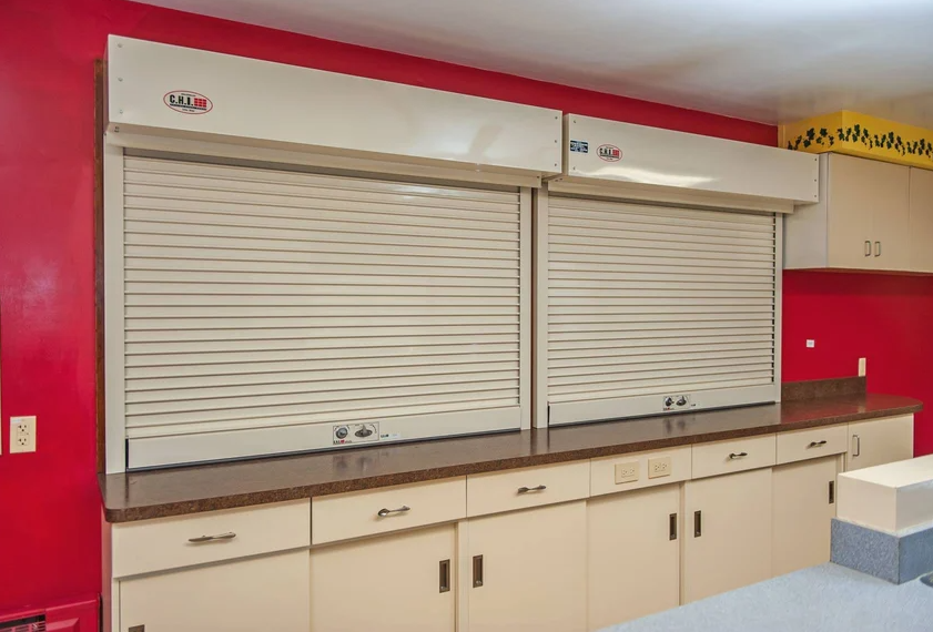 Two beige roll-up security shutters closed over a counter in a room with red walls.