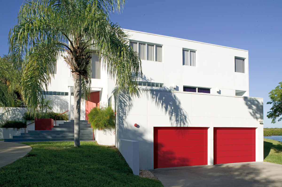 Modern white home with bold red flush-panel garage doors and lush palm trees in the landscape.