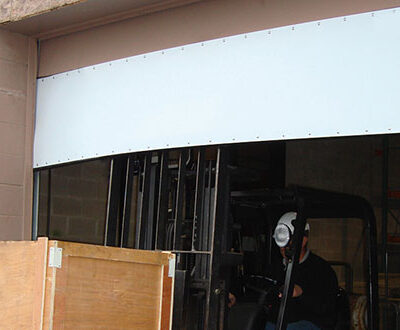 A forklift operated by a person wearing a face mask is exiting a warehouse through a large open Amarr Superflex fitted