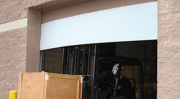 A forklift operated by a person wearing a face mask is exiting a warehouse through a large open Amarr Superflex fitted